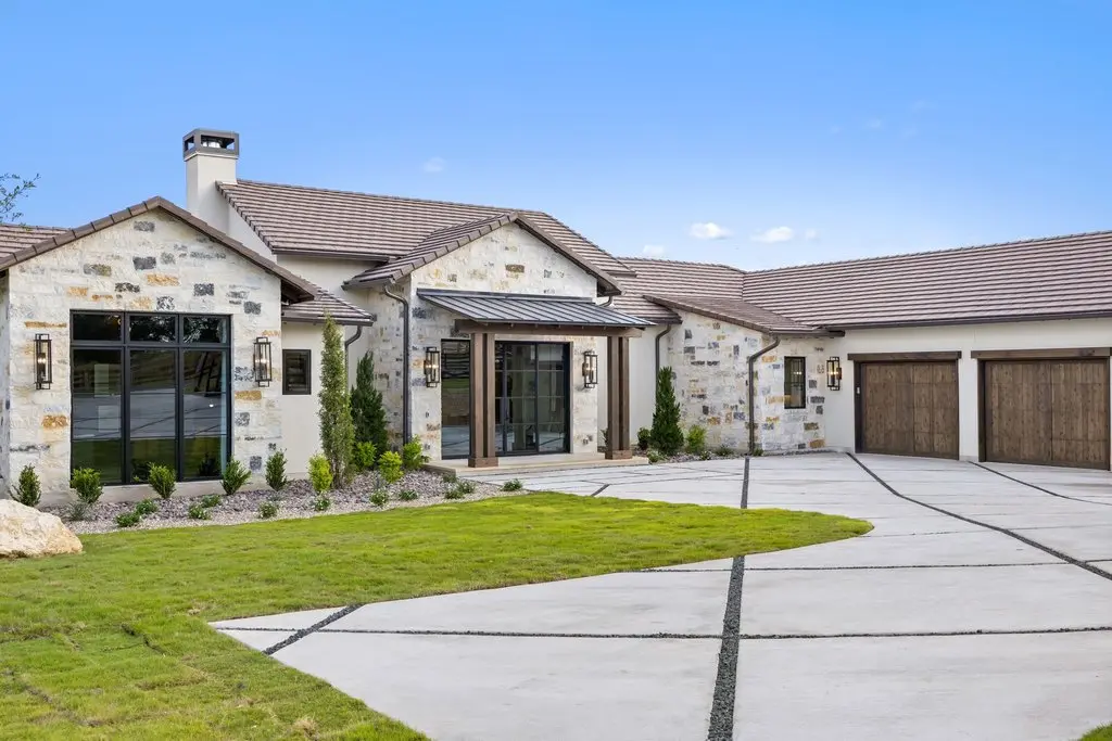 Front elevation of a limestone house with a tile roof, timber entry canopy and three garage bays off a wide concrete drive.