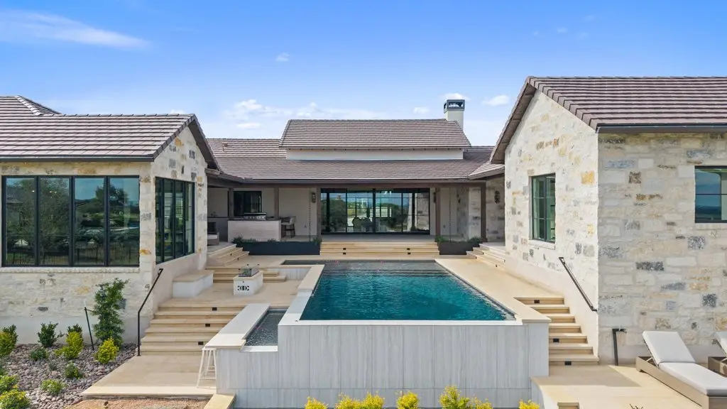 Front elevation of a limestone home with a tile roof, timber entry canopy and three garage bays off a wide concrete drive.
