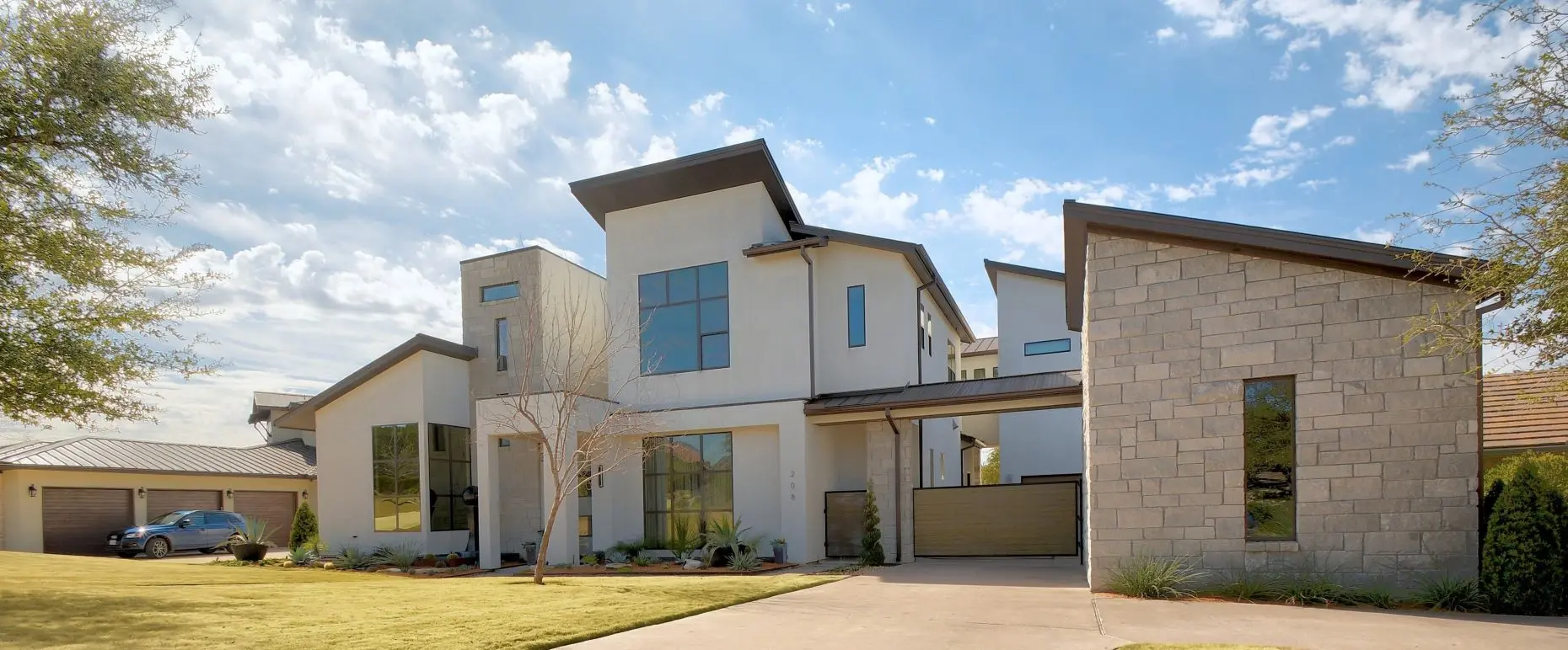 Street elevation of a contemporary house in white stucco and limestone, with black-framed windows and a bare tree in the front yard.