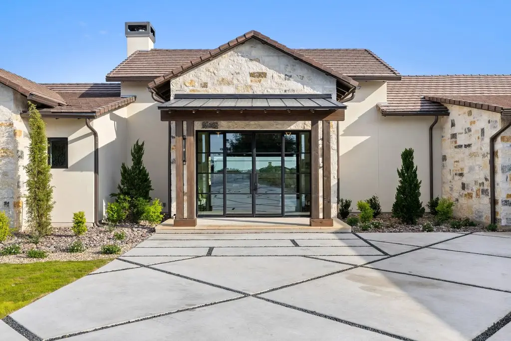 Front elevation of a limestone home with a tile roof, timber entry canopy and three garage bays off a wide concrete drive.