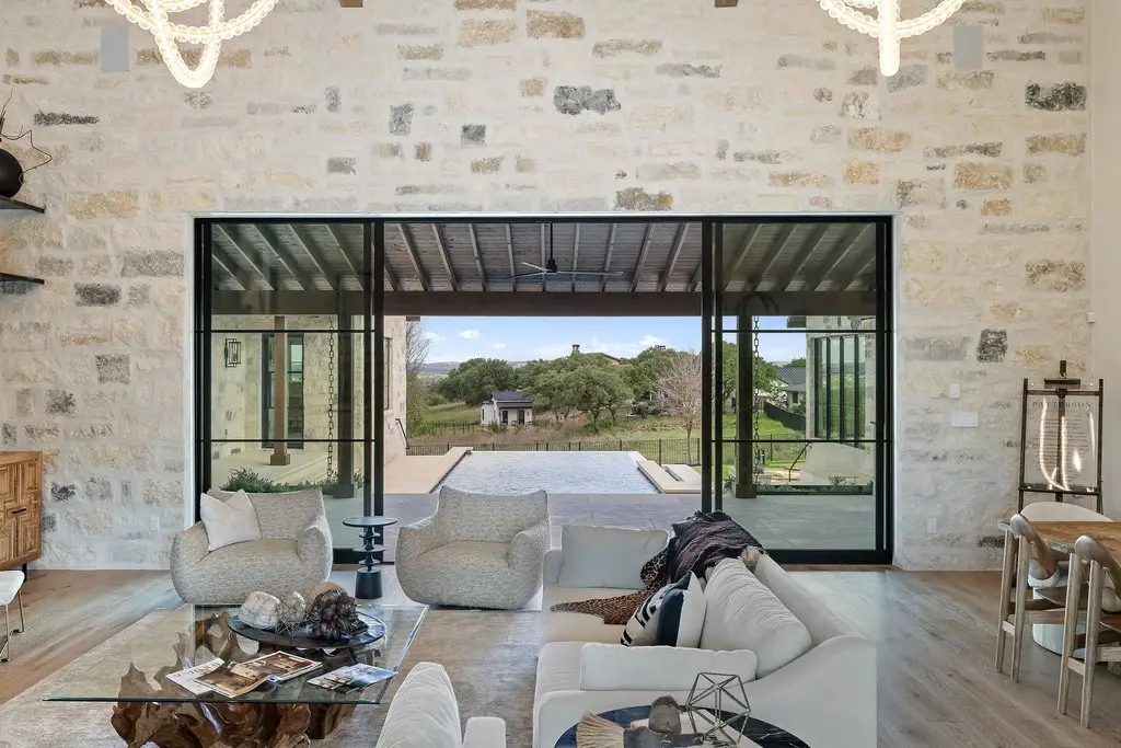 Front elevation of a limestone home with a tile roof, timber entry canopy and three garage bays off a wide concrete drive.