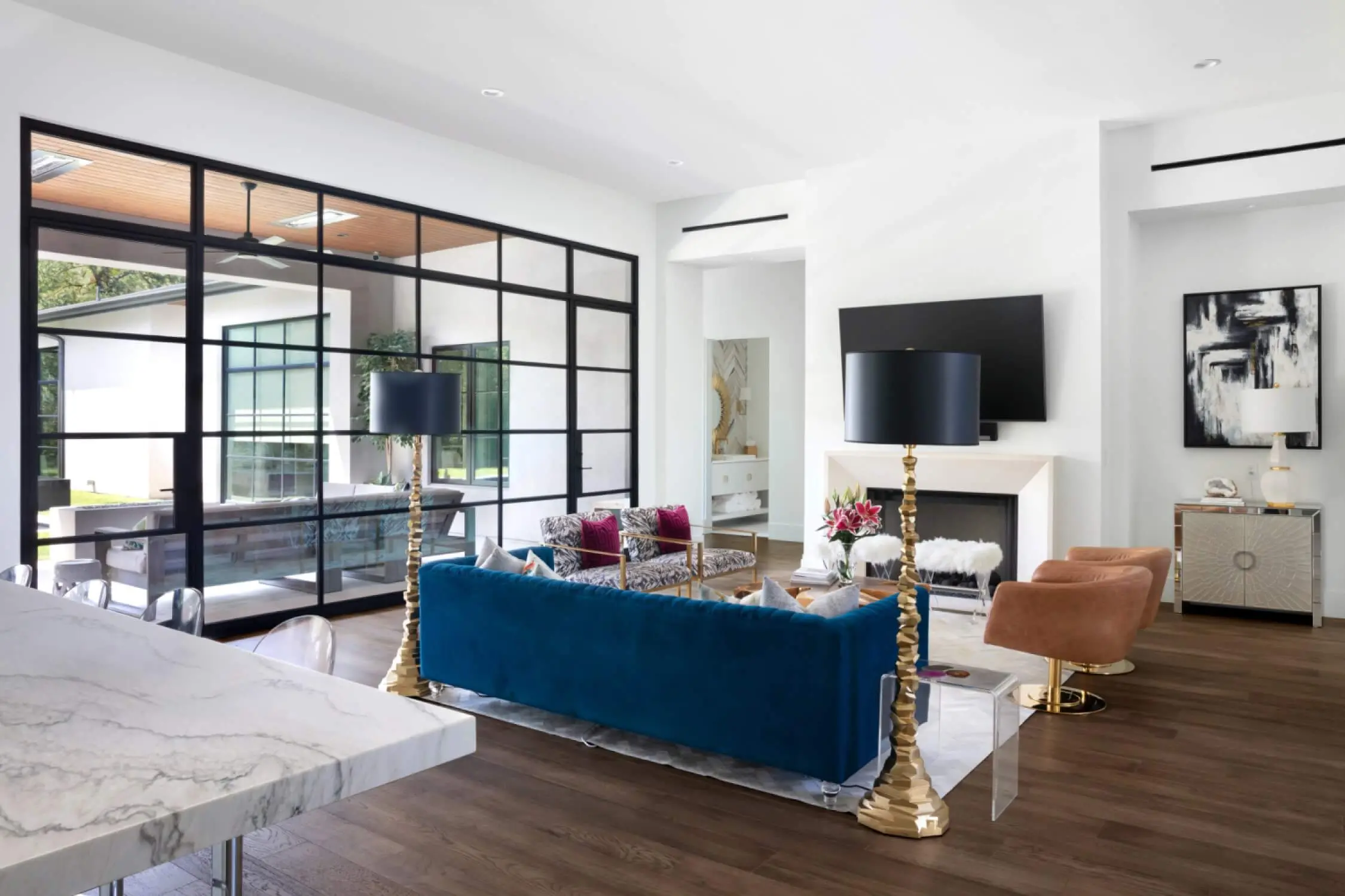 Living room with steel-framed glass partitions, a plaster fireplace and a blue velvet sofa on wide plank floors.