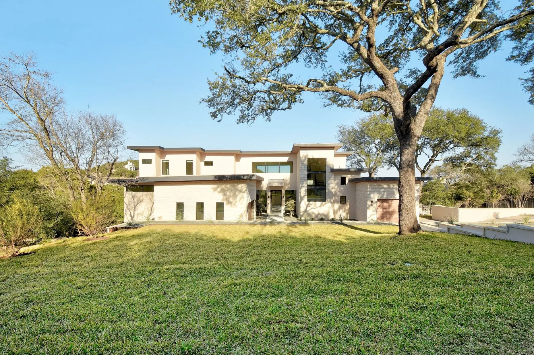 A low white home seen across a wide mown lawn, framed by the spreading branches of a live oak.