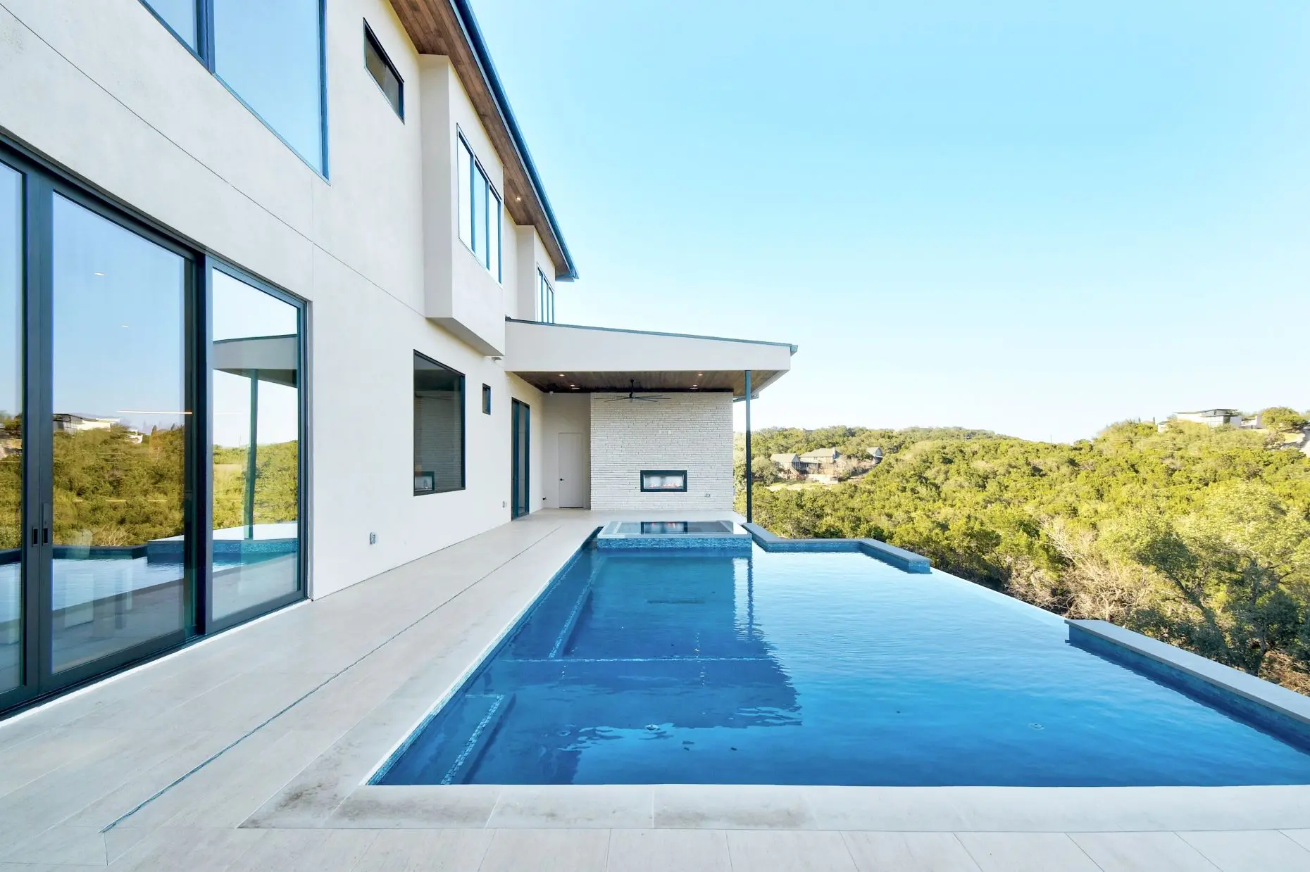 Infinity pool running along the side of a white modern house, looking out over wooded hills.