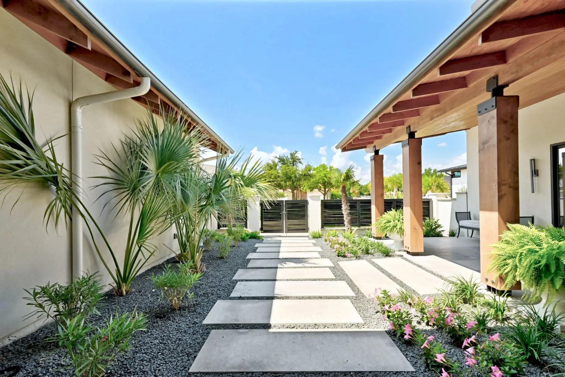 Front elevation behind a circular planted motor court, with a broad stone and stucco facade and palms to one side.