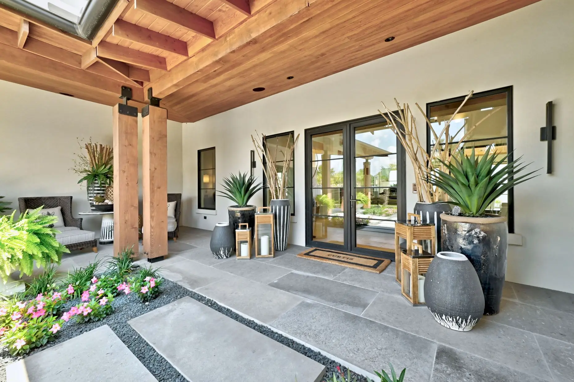 Front elevation behind a circular planted motor court, with a broad stone and stucco facade and palms to one side.