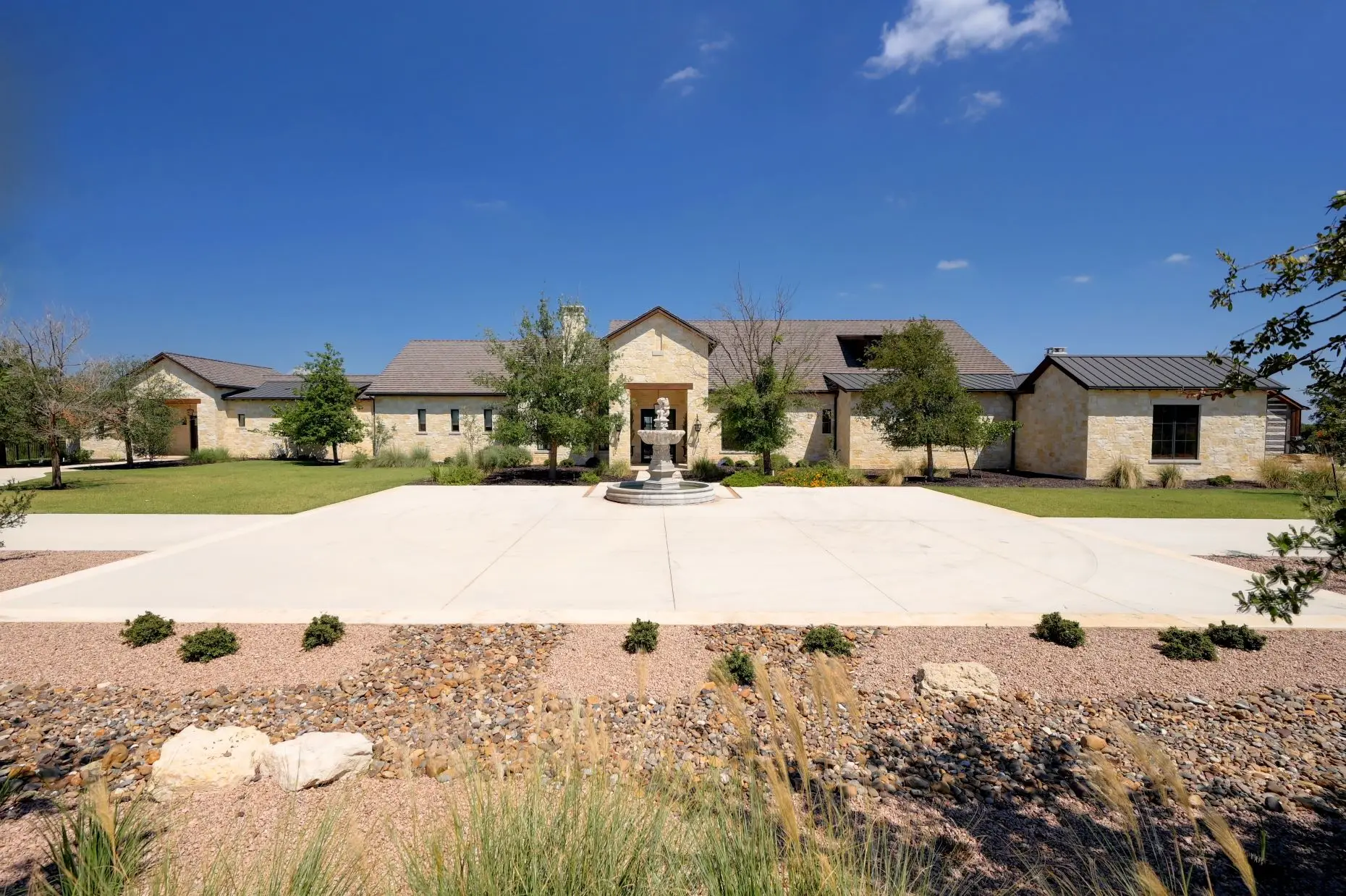 Aerial view of a stone ranch home set around a fountain courtyard, with clipped lawns and open country beyond.