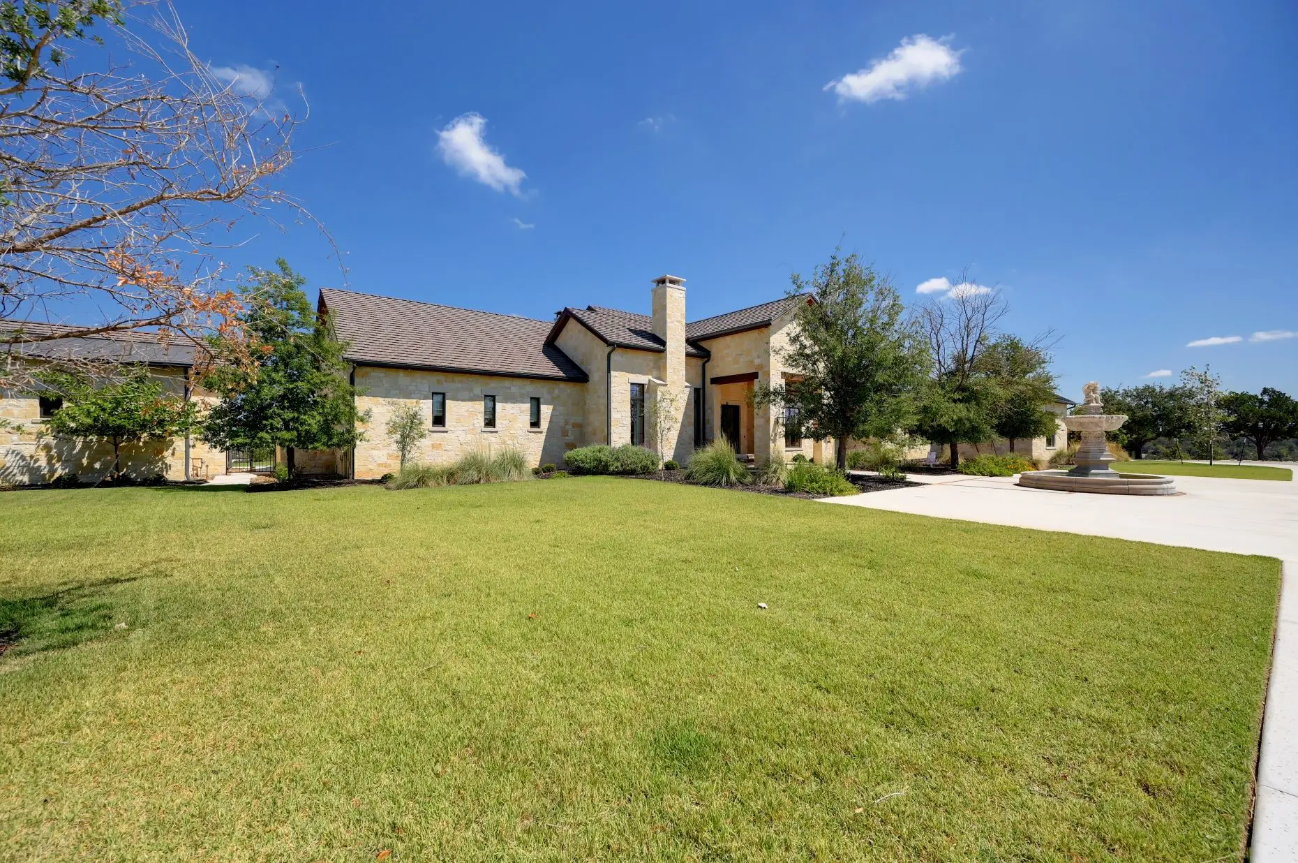 Aerial view of a stone ranch home set around a fountain courtyard, with clipped lawns and open country beyond.