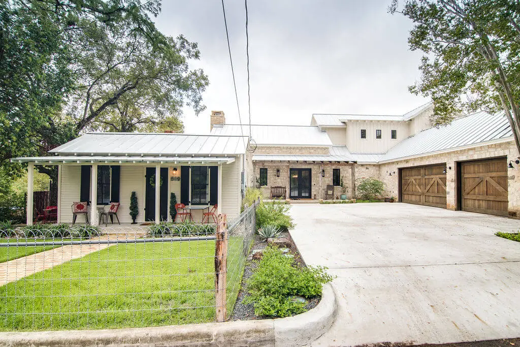 Limestone entry courtyard with a timber-framed porch, black double doors and reclaimed wood garage doors under a standing seam roof.