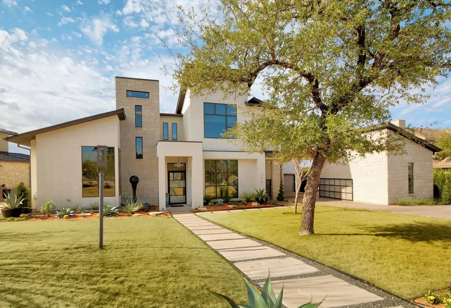 Street elevation of a contemporary home in white stucco and limestone, with black-framed windows and a bare tree in the front yard.
