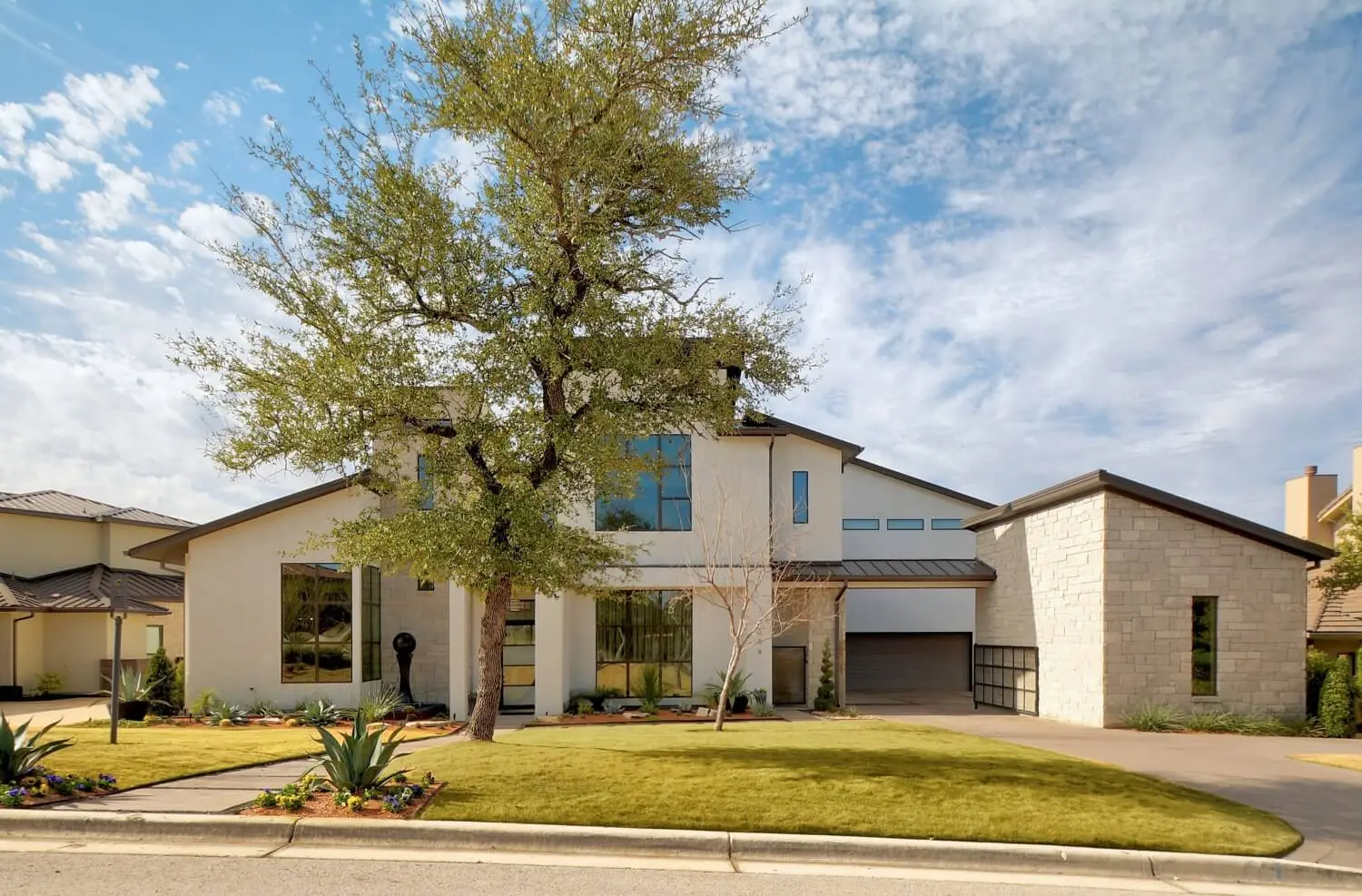 Street elevation of a contemporary home in white stucco and limestone, with black-framed windows and a bare tree in the front yard.