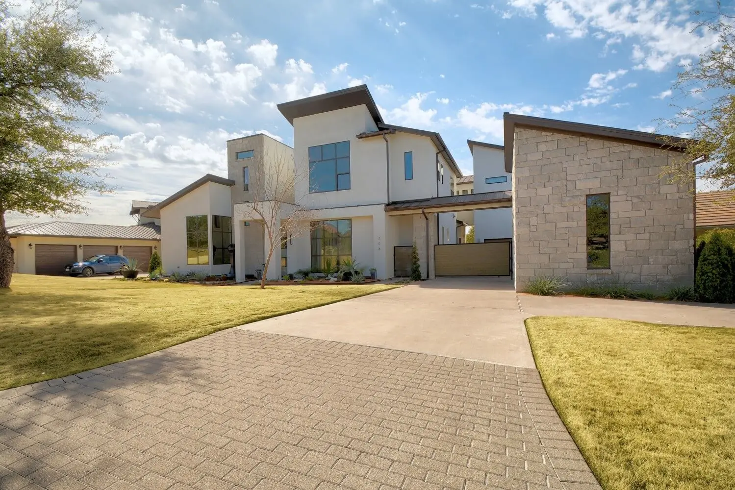 Street elevation of a contemporary home in white stucco and limestone, with black-framed windows and a bare tree in the front yard.