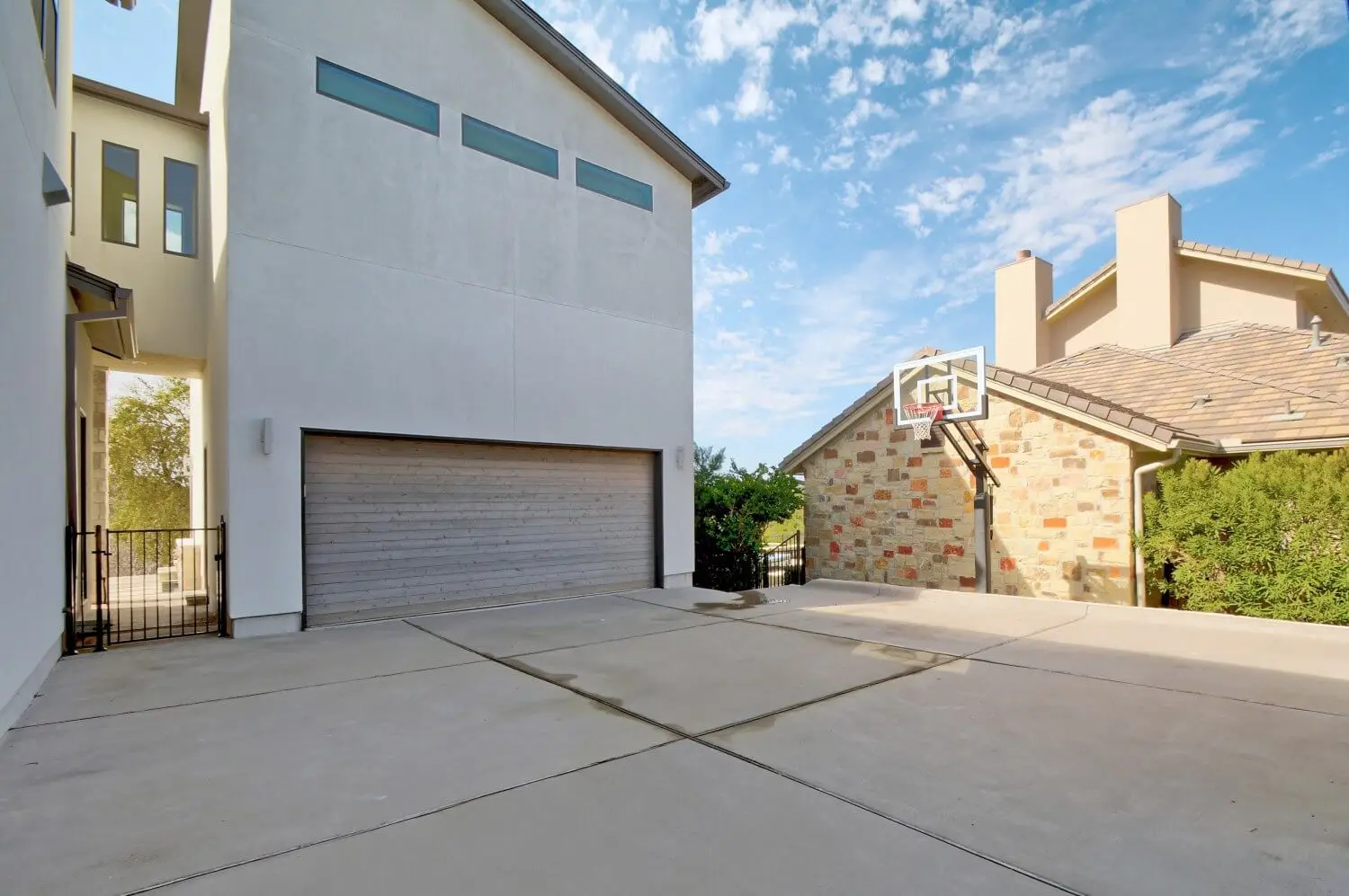 Street elevation of a contemporary home in white stucco and limestone, with black-framed windows and a bare tree in the front yard.