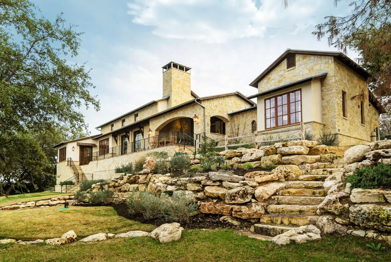 Limestone house stepping up a terraced slope, with a tall chimney and stacked stone retaining walls.
