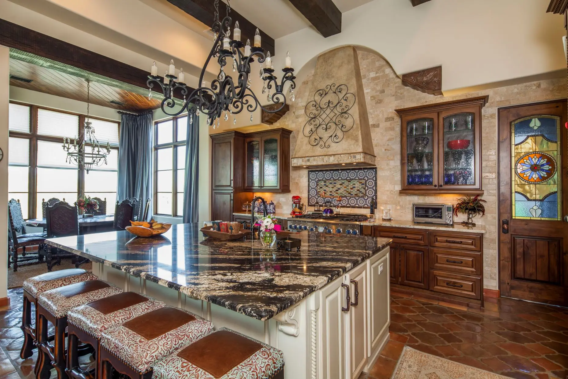 Great room under a beamed ceiling, with a carved stone fireplace, arched openings and a wall of built-in cabinets.