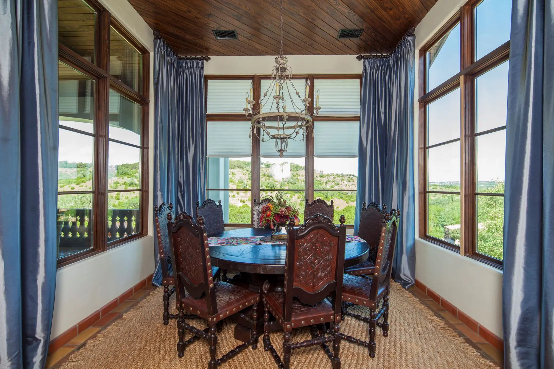 Great room under a beamed ceiling, with a carved stone fireplace, arched openings and a wall of built-in cabinets.