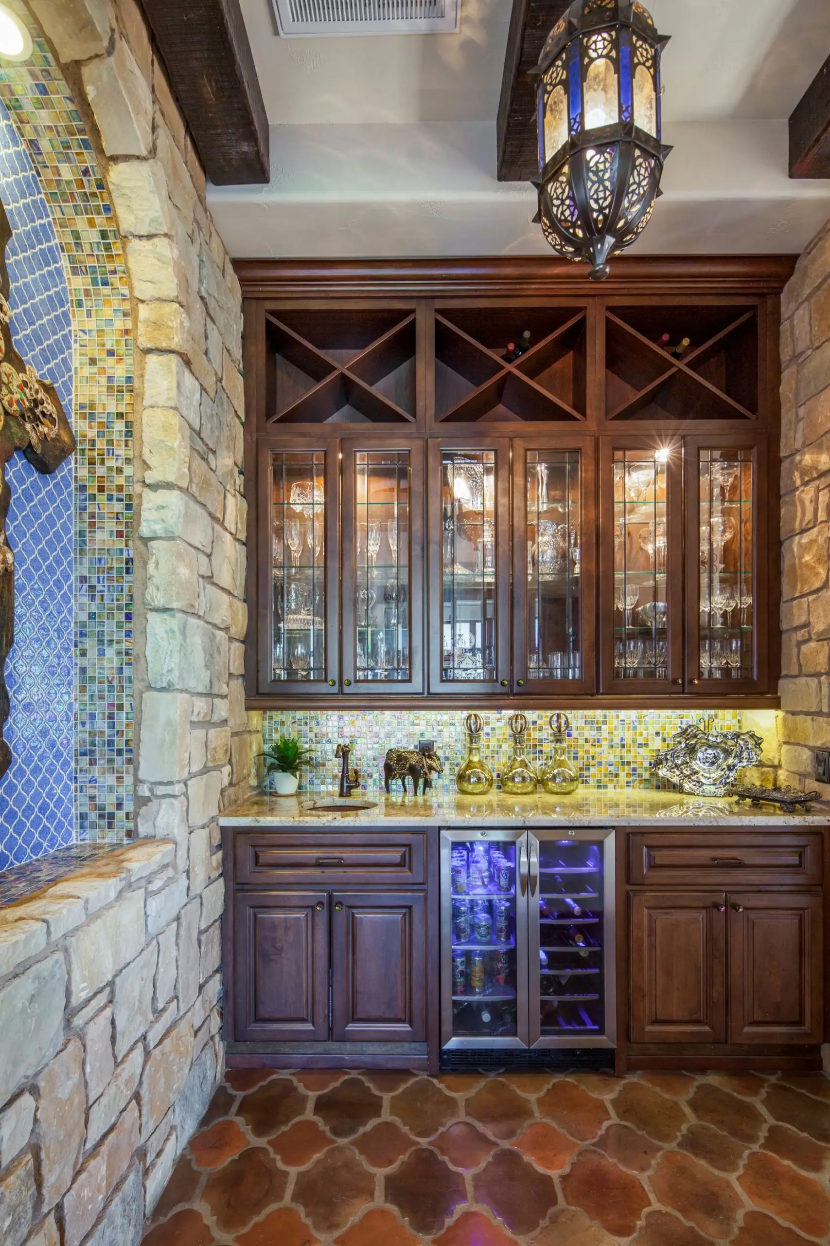 Great room under a beamed ceiling, with a carved stone fireplace, arched openings and a wall of built-in cabinets.