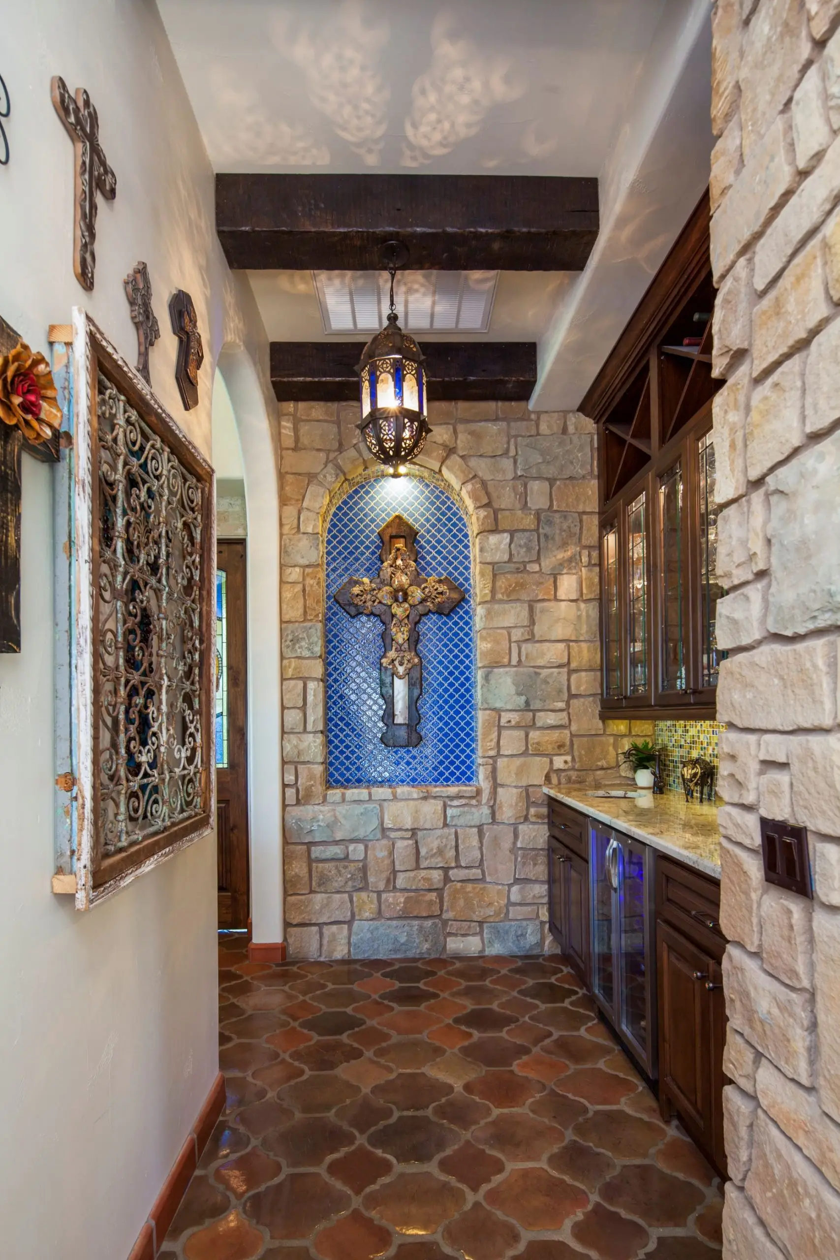Great room under a beamed ceiling, with a carved stone fireplace, arched openings and a wall of built-in cabinets.