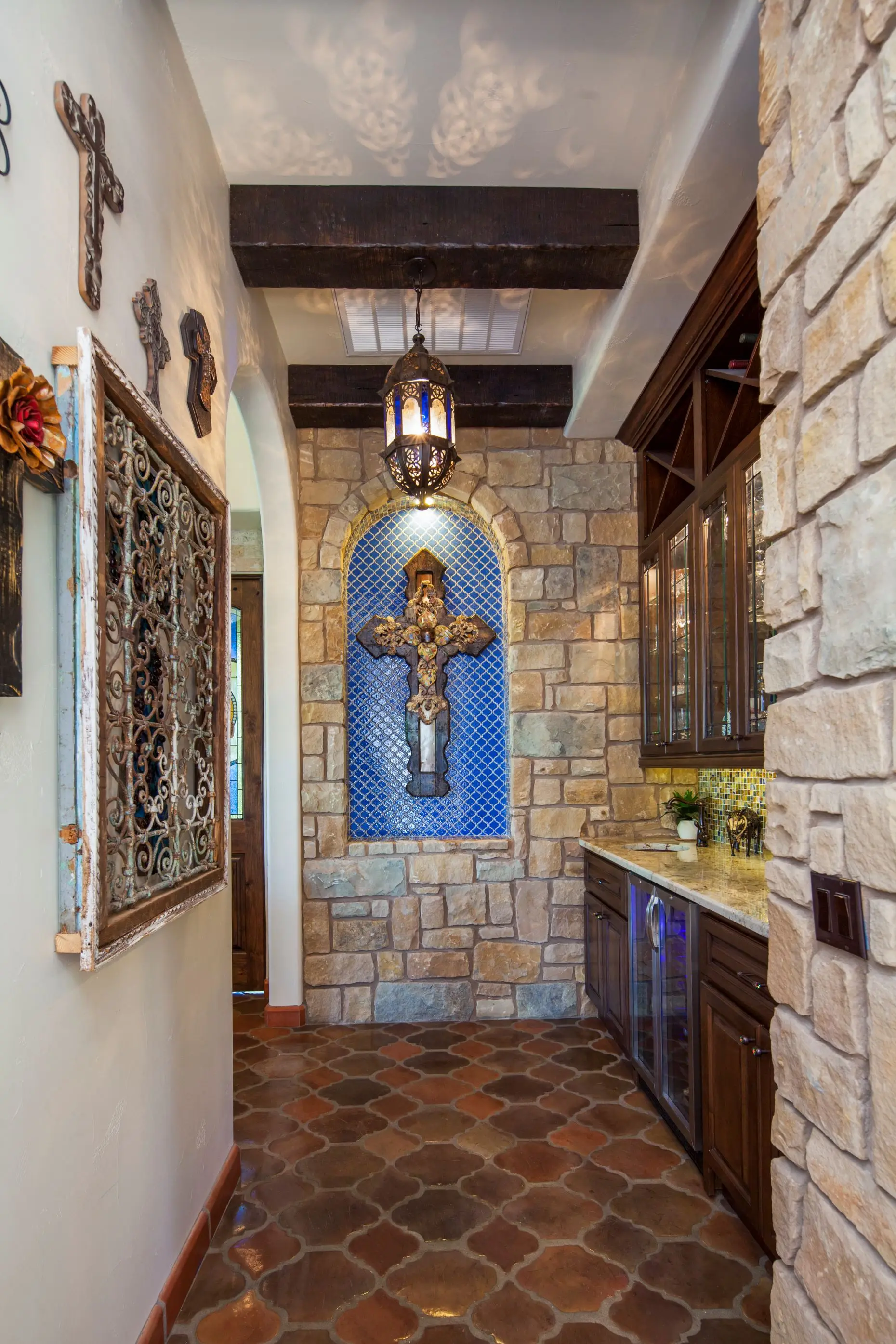 Great room under a beamed ceiling, with a carved stone fireplace, arched openings and a wall of built-in cabinets.