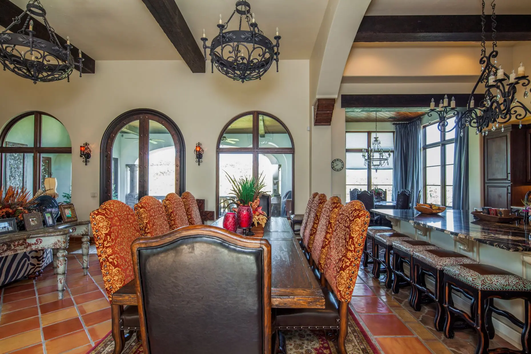 Great room under a beamed ceiling, with a carved stone fireplace, arched openings and a wall of built-in cabinets.