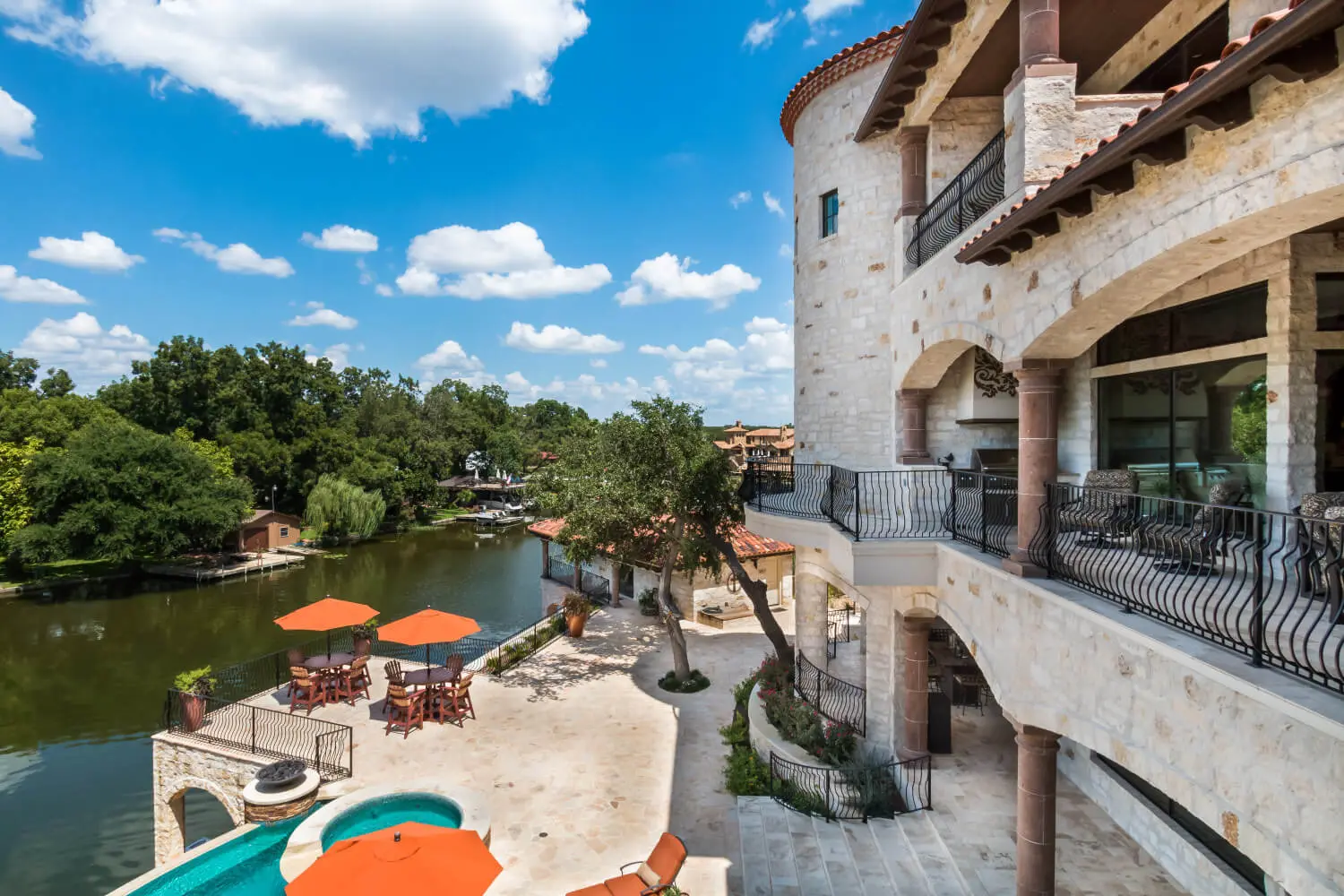 Tuscan-style villa with tile roofs and a stone terrace, seen across still water from the far bank.