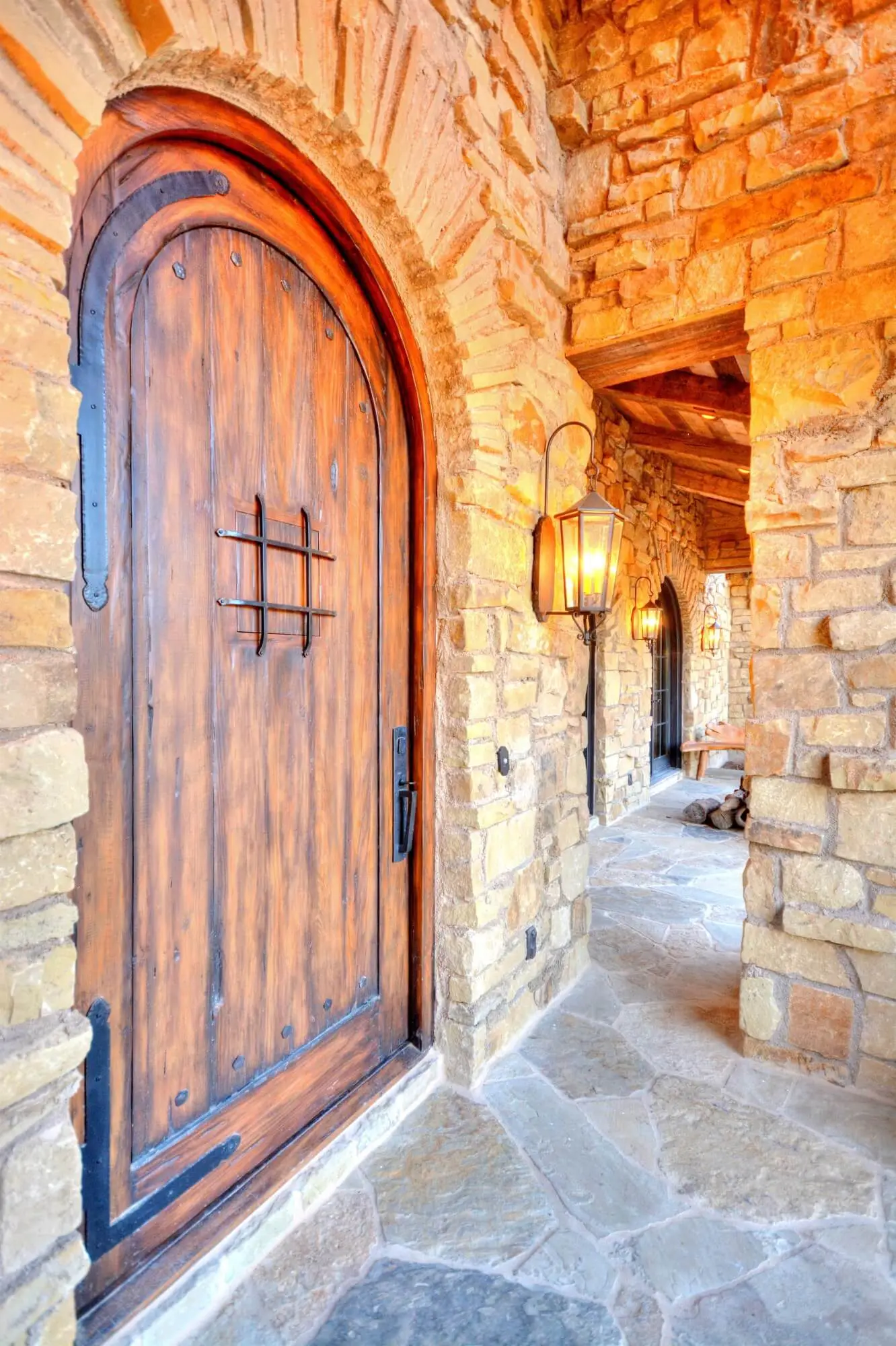 Stone ranch home at dusk with a tile roof and lit arcade, behind a gravel bed and large clay urns in the motor court.