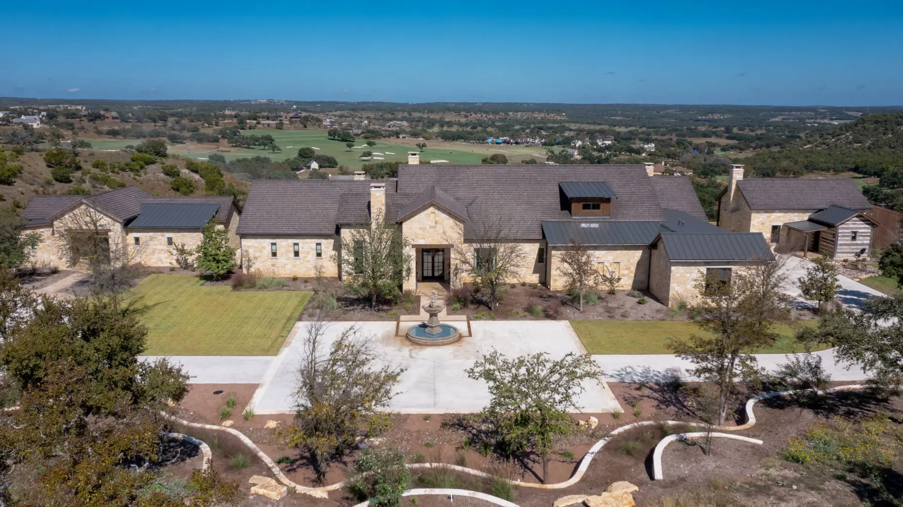 Aerial view of a stone ranch house set around a fountain courtyard, with clipped lawns and open country beyond.