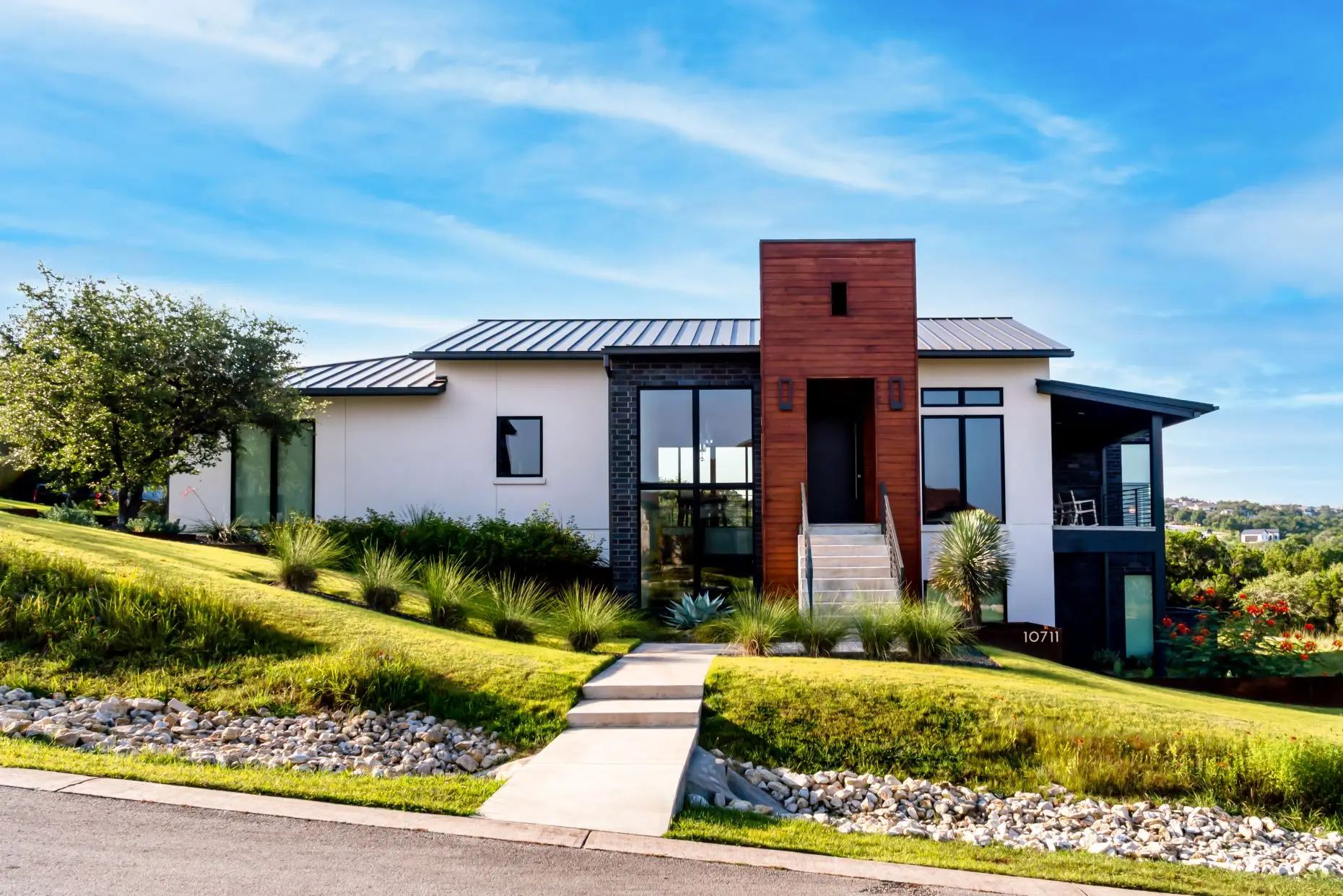 Street elevation at dusk of a low modern home with dark cladding and a metal roof, set above a sloping drive.