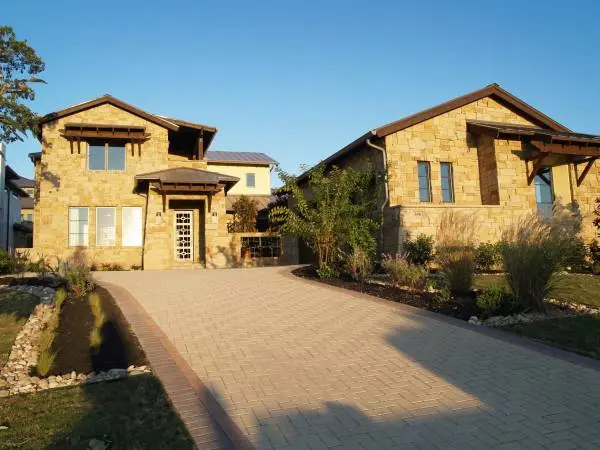 Stone entry elevation lit at dusk, with a shed-roofed porch, tall windows and a low wall along the walk.