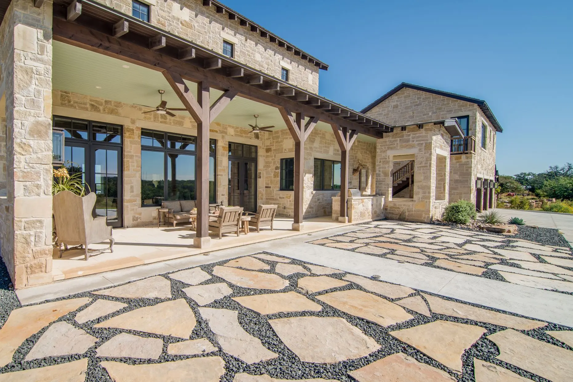 Stone loggia on timber posts running along the rear of the house, above a flagstone terrace set in gravel.