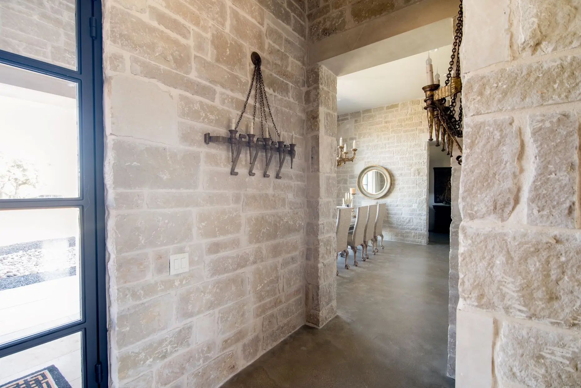 Stone loggia on timber posts running along the rear of the home, above a flagstone terrace set in gravel.