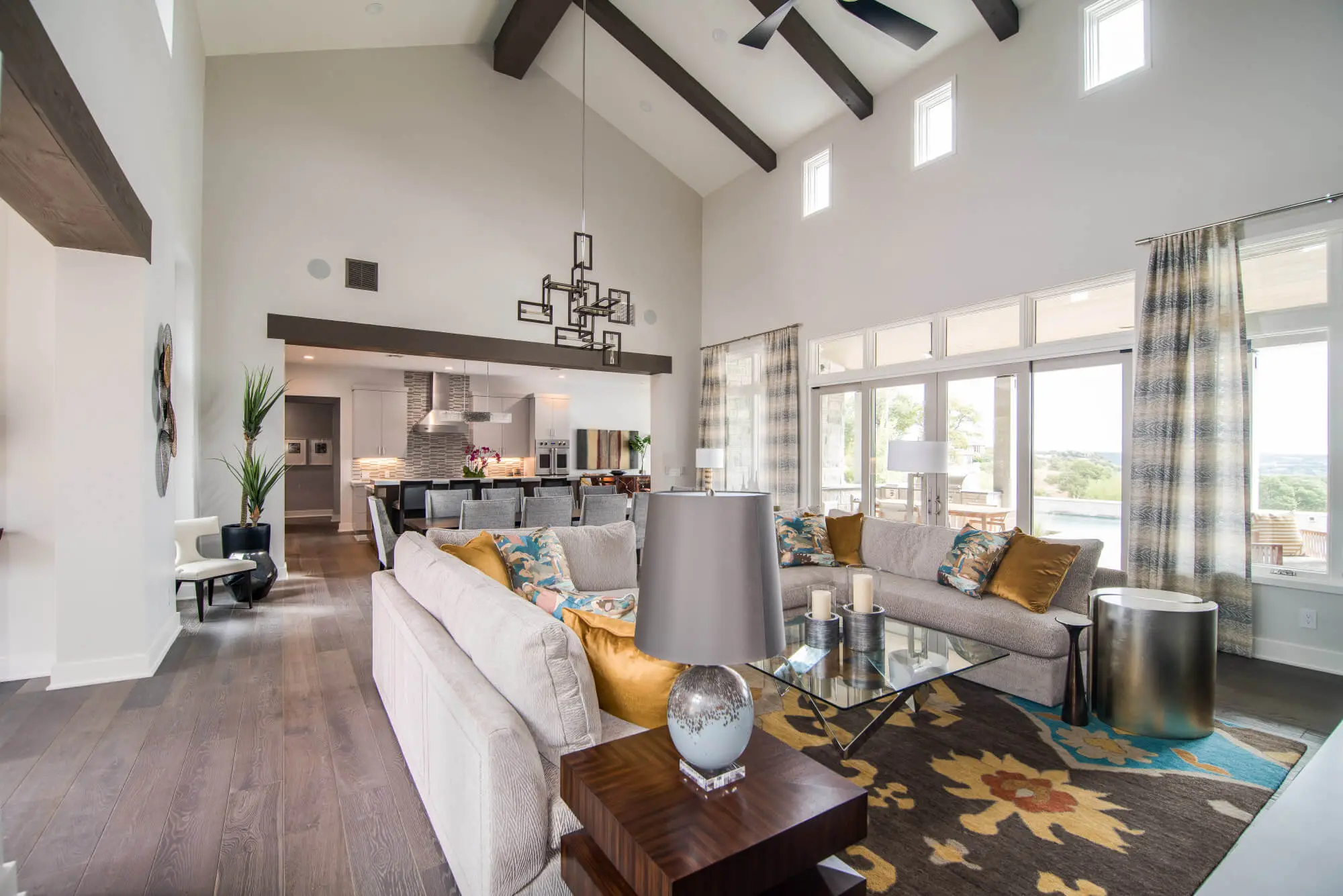 Living room with a full-height stone fireplace, exposed beams and a glass door standing open to the view beyond.