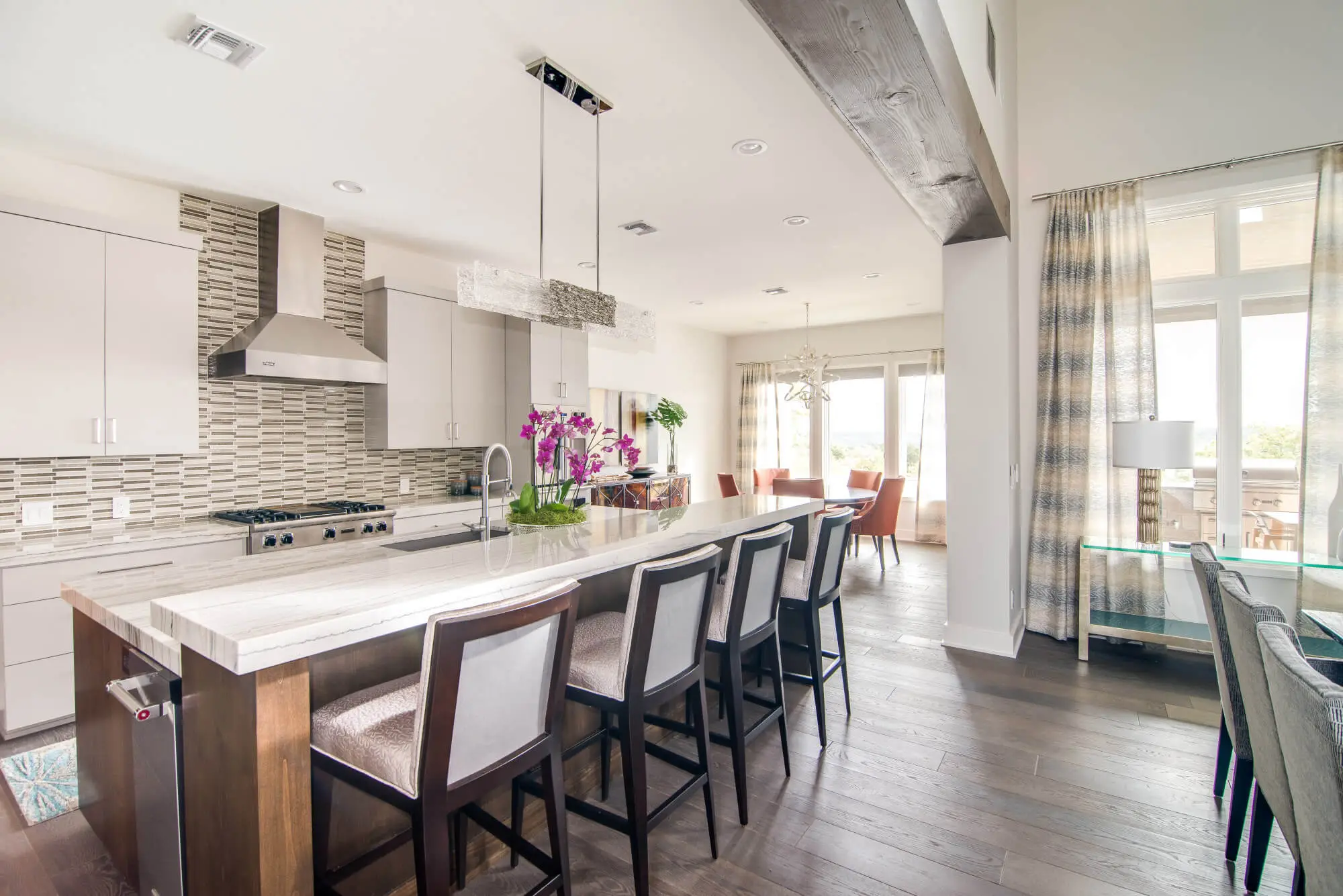 Living room with a full-height stone fireplace, exposed beams and a glass door standing open to the view beyond.