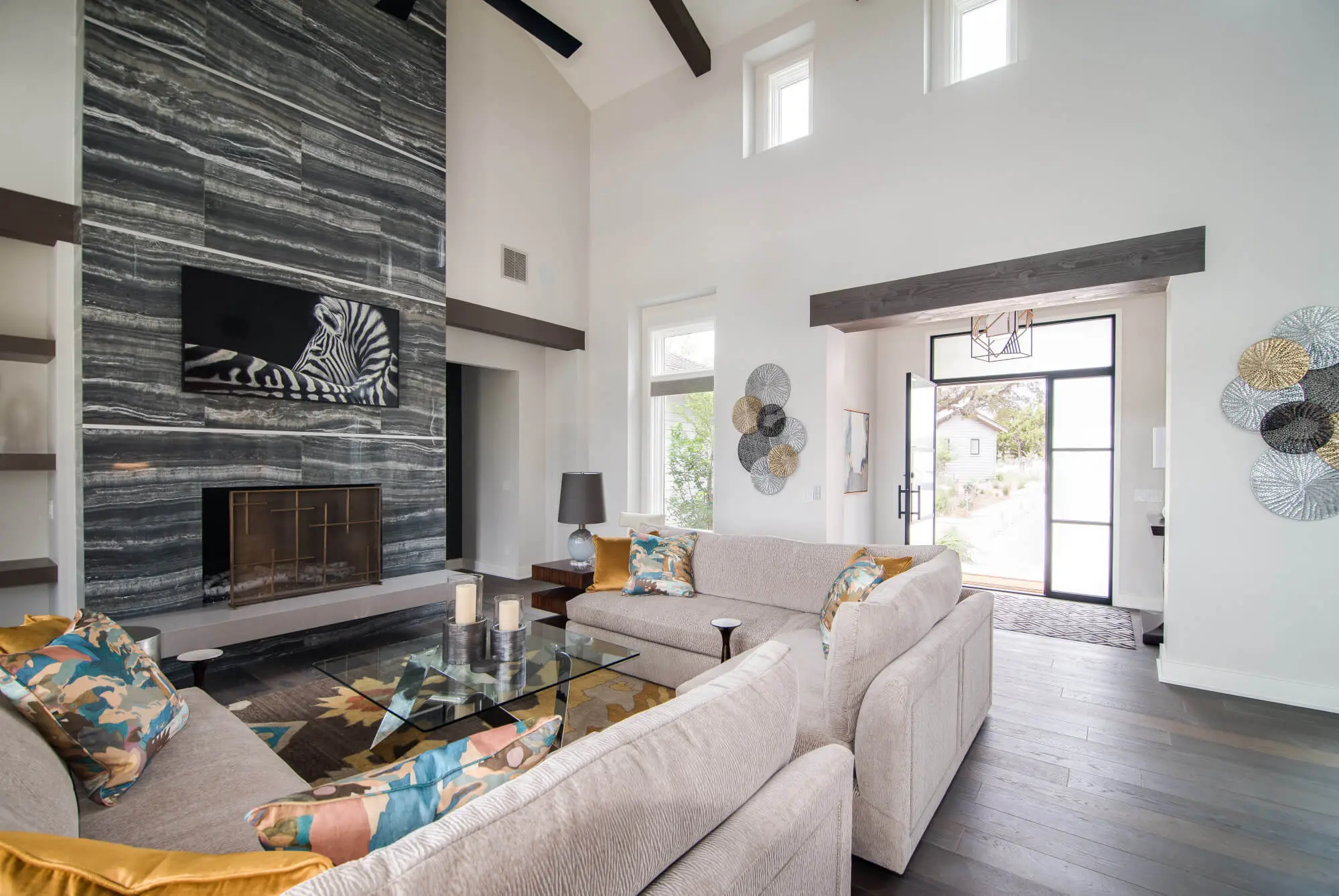Living room with a full-height stone fireplace, exposed beams and a glass door standing open to the view beyond.