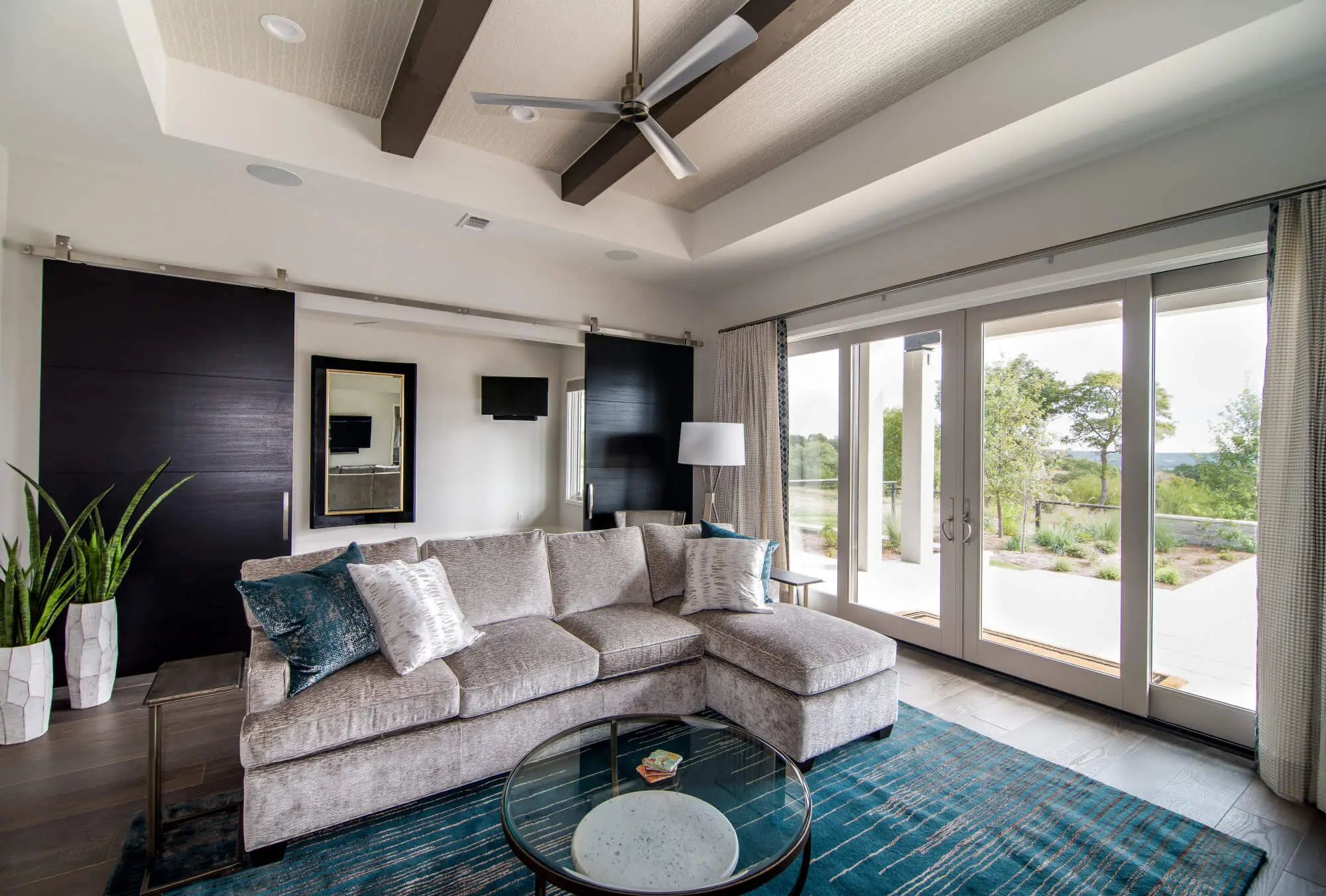 Living room with a full-height stone fireplace, exposed beams and a glass door standing open to the view beyond.