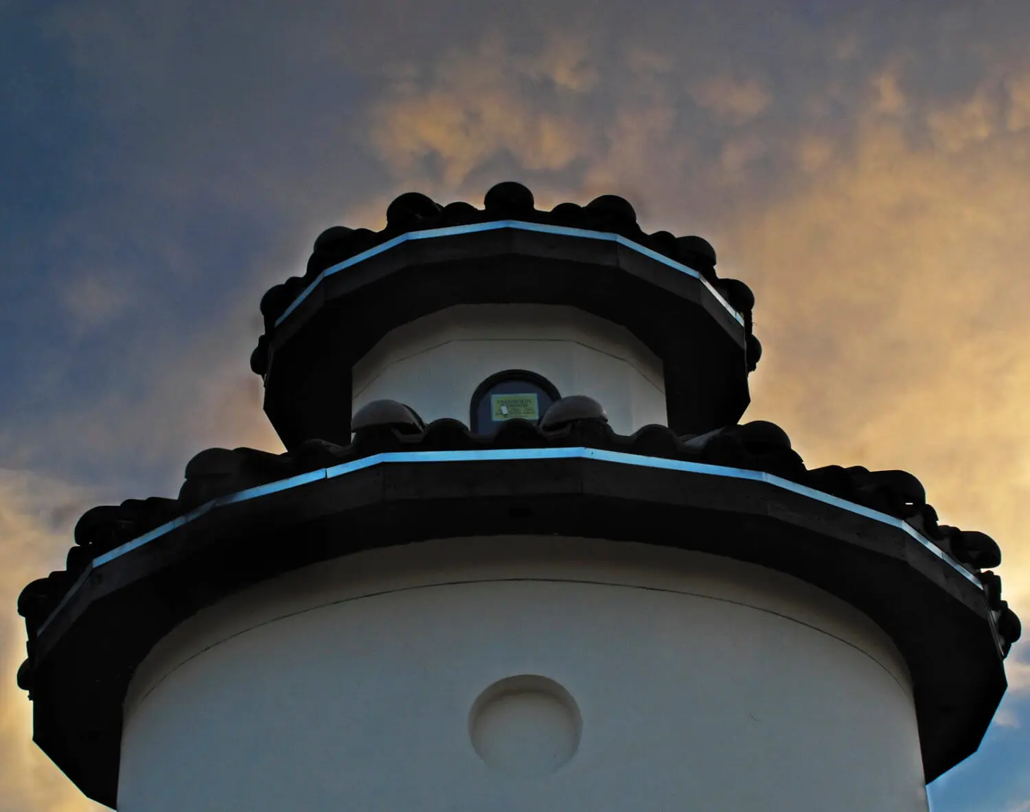 Front elevation at dusk of a Mediterranean home with a stucco turret, tile roof and lit arched entry above a curved drive.