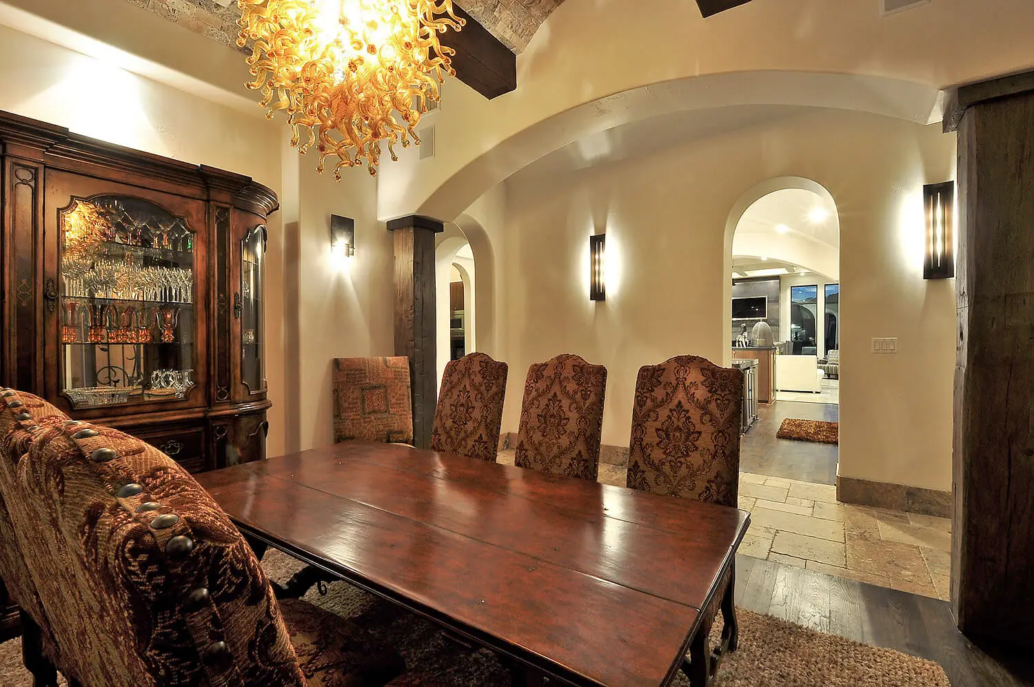 Front elevation at dusk of a Mediterranean home with a stucco turret, tile roof and lit arched entry above a curved drive.