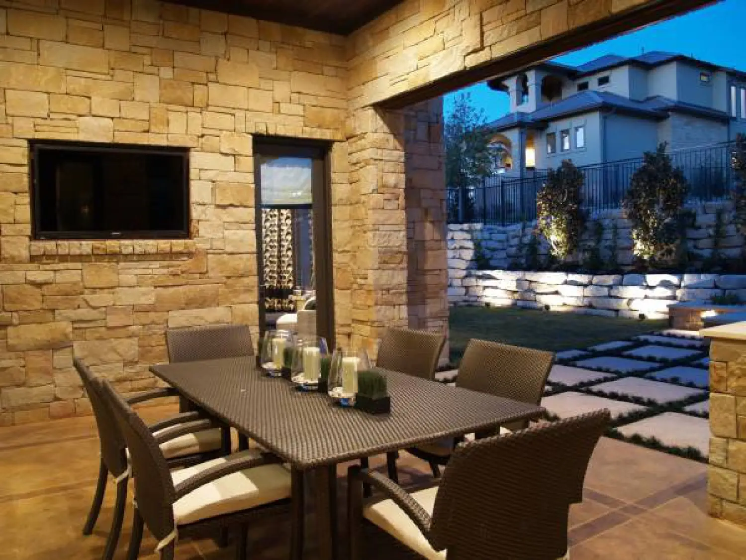 Stone entry elevation lit at dusk, with a shed-roofed porch, tall windows and a low wall along the walk.