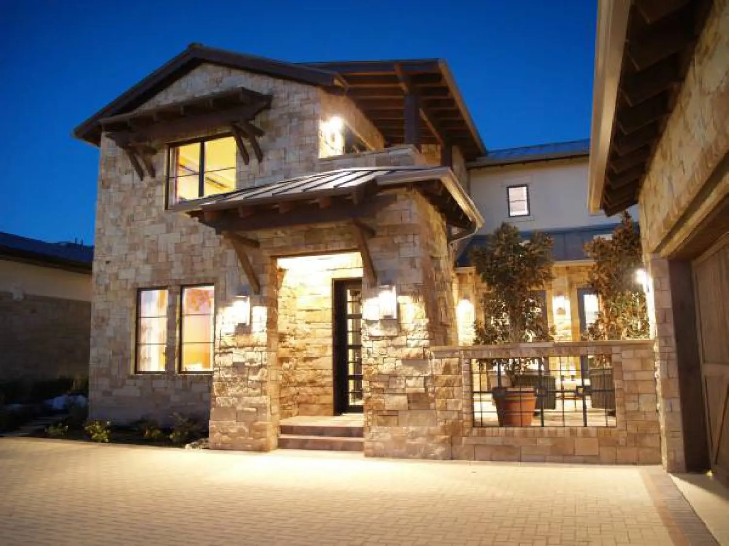 Stone entry elevation lit at dusk, with a shed-roofed porch, tall windows and a low wall along the walk.