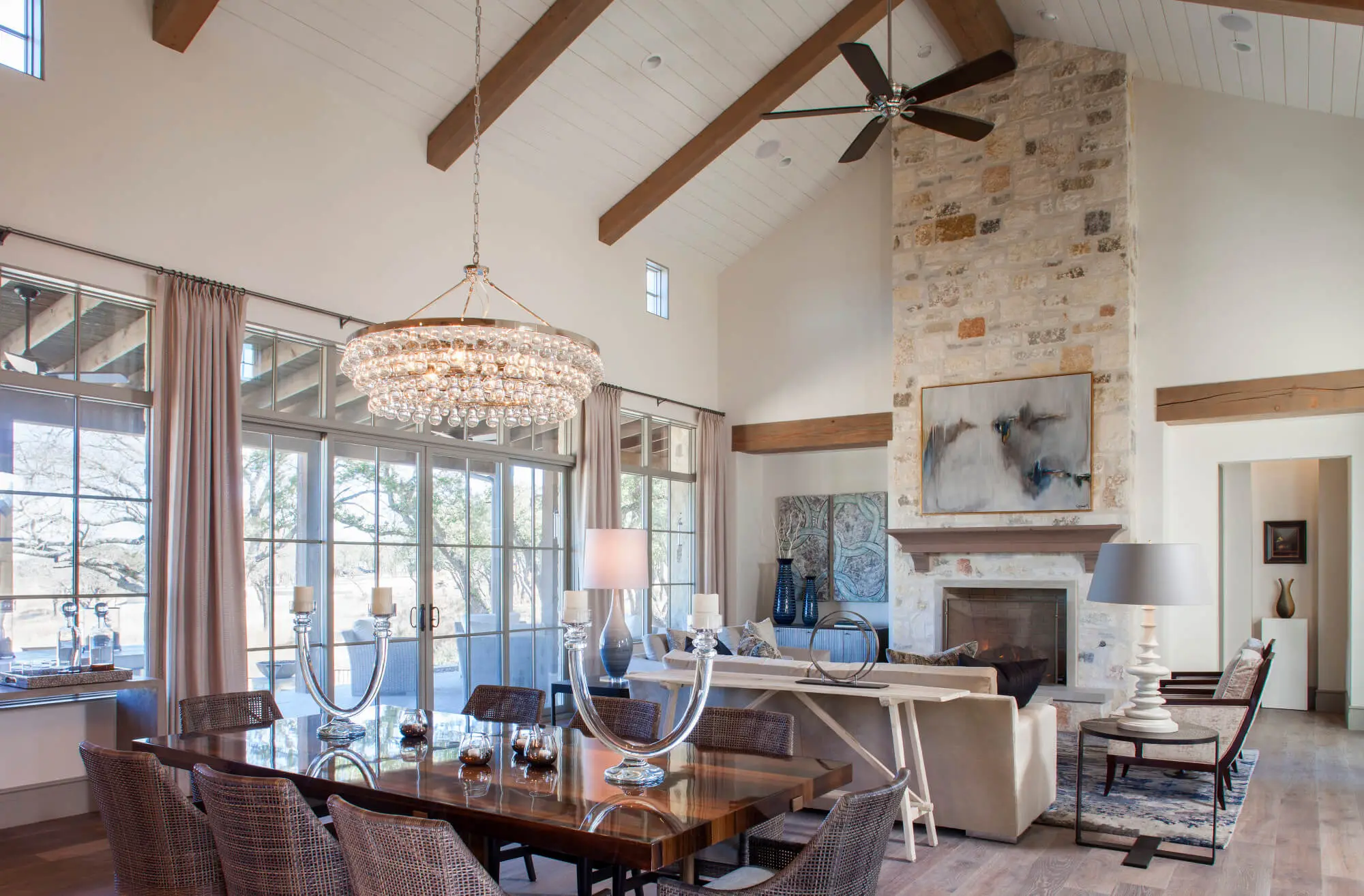 A vaulted living room with exposed beams and a stone chimney breast, opening through tall windows onto a covered porch.