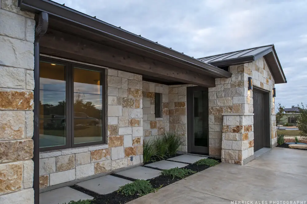 Front elevation of a two-story stone and stucco home with two garage bays and planted beds along the drive.