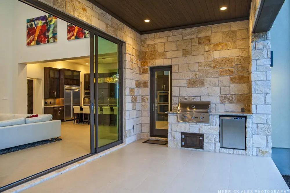 Front elevation of a two-story stone and stucco home with two garage bays and planted beds along the drive.