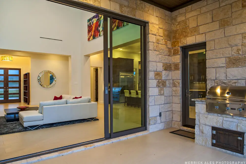 Front elevation of a two-story stone and stucco home with two garage bays and planted beds along the drive.