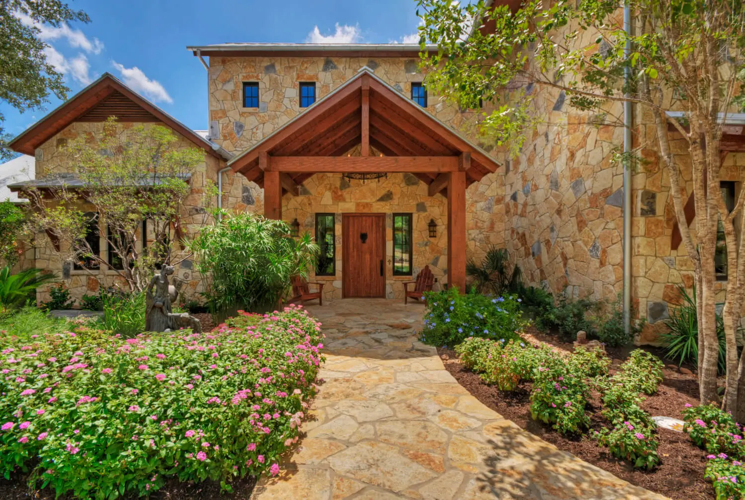 Two-story stone and timber home with a standing seam metal roof, framed by oaks above a clipped lawn.