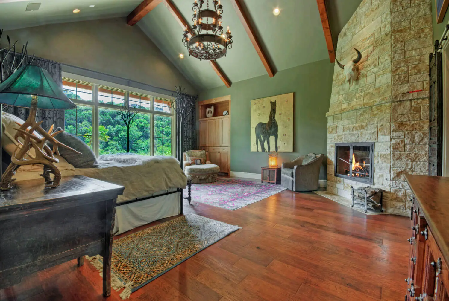 Two-story stone and timber home with a standing seam metal roof, framed by oaks above a clipped lawn.