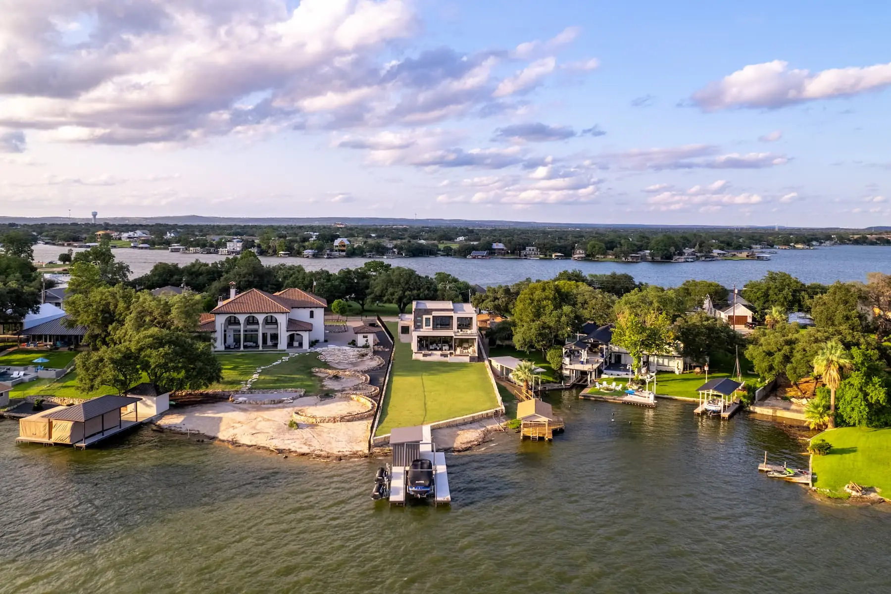 Lakefront elevation seen from the water, with a boat dock, a wide lawn and the home standing at the top of the bank.