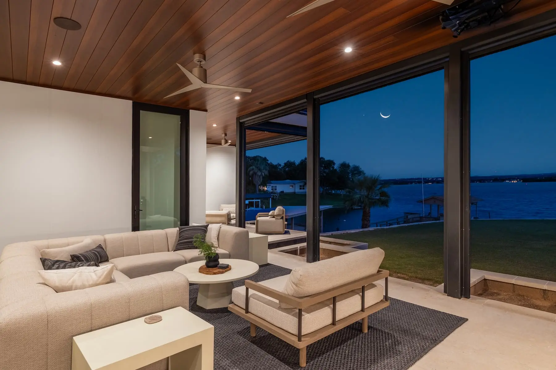 Lakefront elevation seen from the water, with a boat dock, a wide lawn and the home standing at the top of the bank.