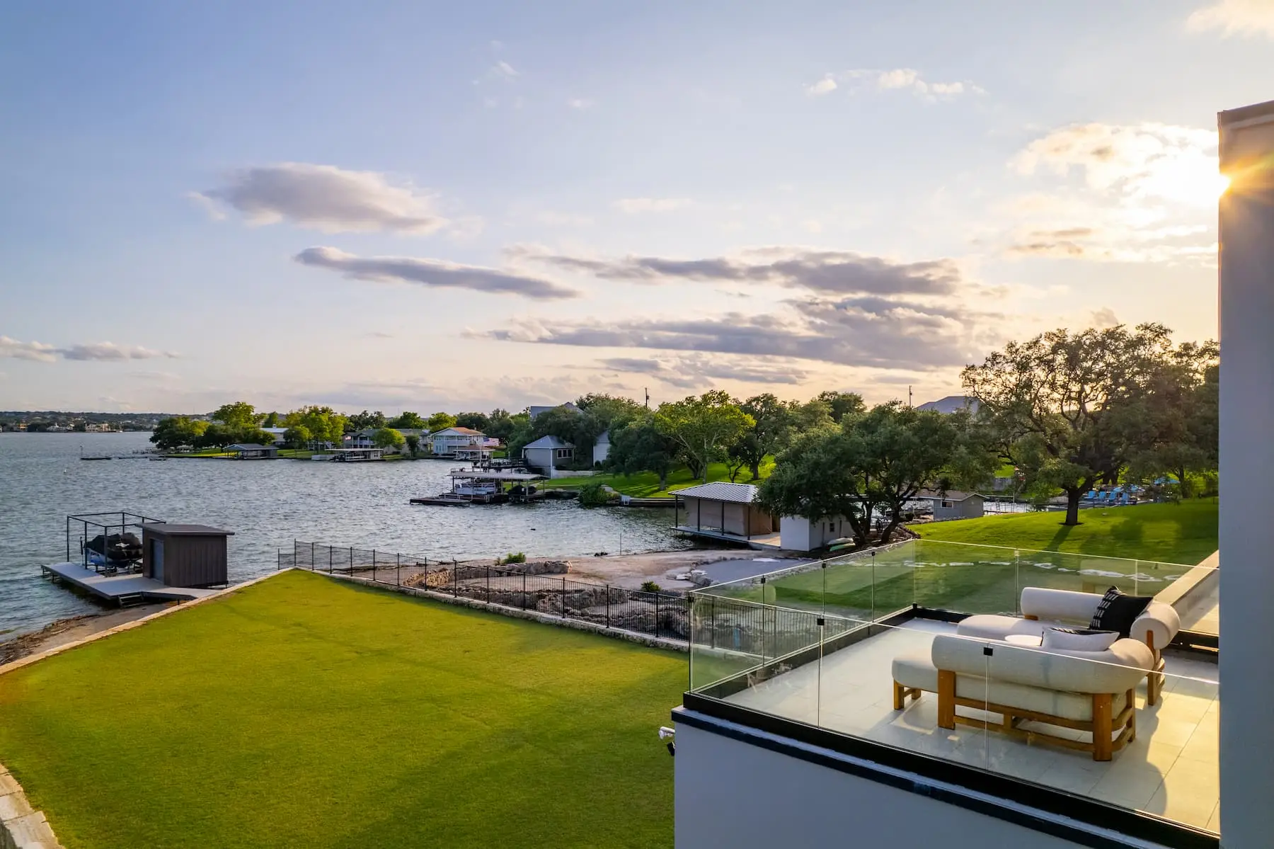 Lakefront elevation seen from the water, with a boat dock, a wide lawn and the home standing at the top of the bank.