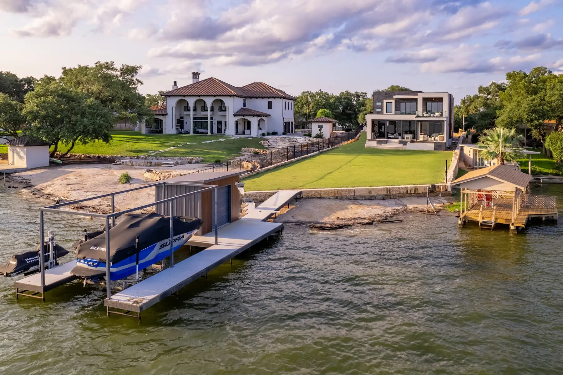 Lakefront elevation seen from the water, with a boat dock, a wide lawn and the house standing at the top of the bank.
