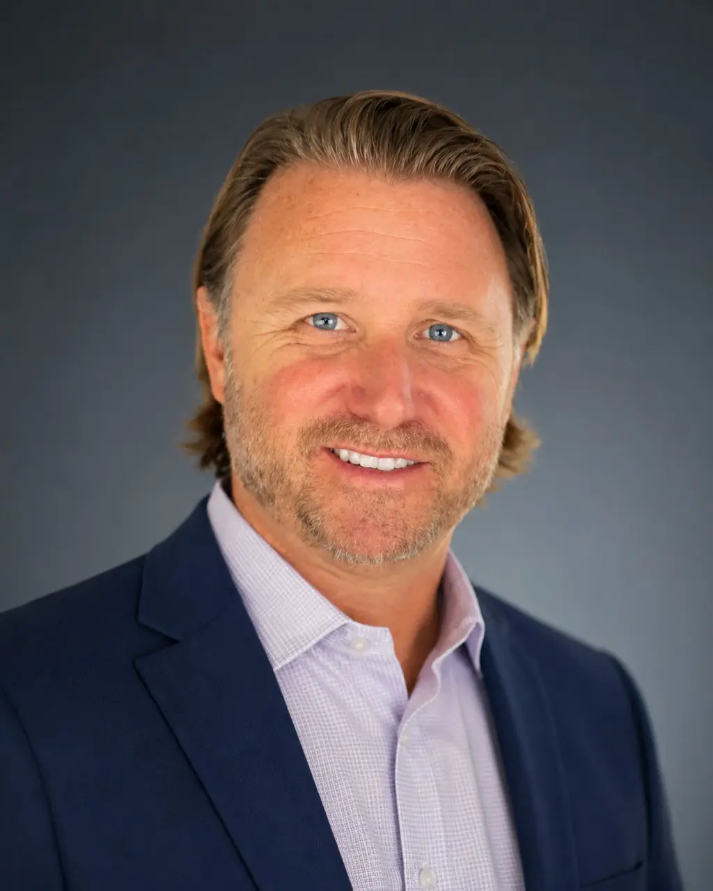 Chad Faucheux, a founding partner of the studio, in a navy jacket and open-necked shirt against a grey studio background.
